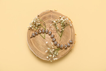 Wooden stand with golden bracelet and flowers on yellow background