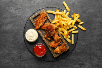 Boards of tasty fried codfish with french fries and sauces on dark background