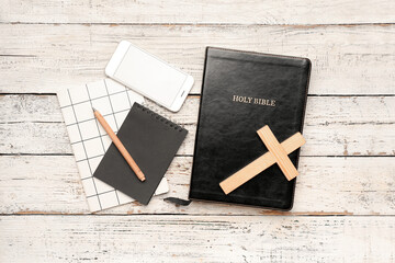 Holy Bible with mobile phone, notebooks and cross on white wooden background