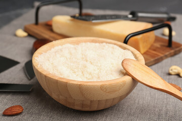 Bowl with tasty grated Parmesan cheese on table, closeup
