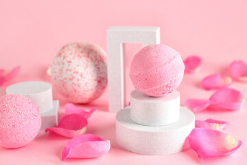 Podiums with bath bombs and floral petals on pink background, closeup