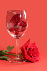 Glass with petals and beautiful rose on red background