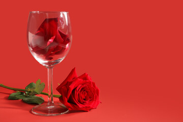 Glass with petals and beautiful rose on red background
