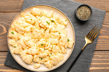 Plate of delicious scrambled eggs with spices on brown wooden background