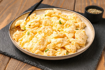 Plate of delicious scrambled eggs with spices on brown wooden background, closeup