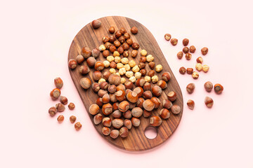 Board with shelled hazelnuts on light background