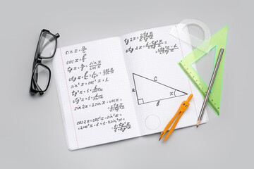Copybook with maths formulas, glasses and stationery on grey background