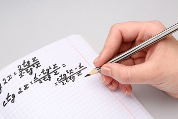 Woman writing maths formulas in copybook with pencil on grey background
