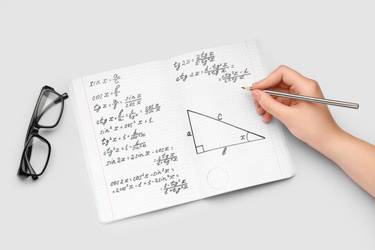 Woman writing maths formulas in copybook with pencil on grey background
