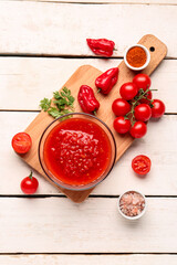 Bowl with tasty tomato sauce and fresh vegetables on light wooden background