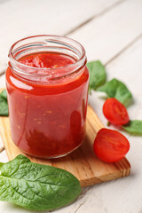 jar with tasty tomato sauce on light wooden background, closeup