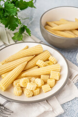 Plate with tasty canned corn cobs on light background