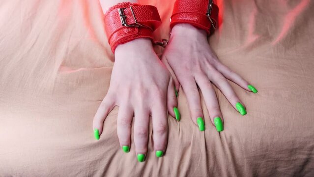 Girl's hands are shackled with red leather handcuffs for role-playing close-up. Gets pleasure, squeezing the sheets with his hands
