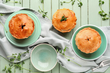 Plates with tasty meat pot pie on green wooden background