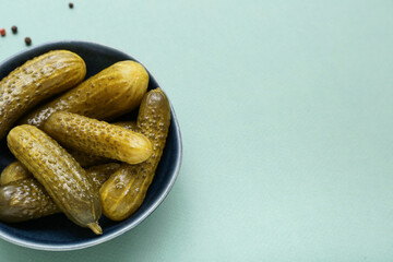 Bowl of tasty canned cucumbers with spices on blue background