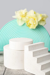 Decorative plaster podiums with daffodils on tile against grey wall