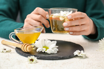 Female hands with cup of tea, honey and beautiful chrysanthemums on white table