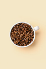 Cup with aromatic coffee beans on pale yellow background
