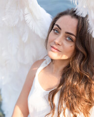 Close portrait of a young woman. Blue-eyed girl with white wings is watching us. White angel. Beautiful lady