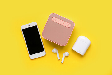 Earphones, speaker and mobile phone on yellow background