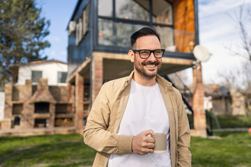 Happy Homeowner Man with Cup of Tea Stand in Front of Modern House