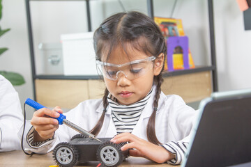 School student making robotic cars. Girl at robotics school makes robot managed from the constructor, child learns robot constructing.