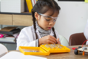 School student making robotic cars. Girl at robotics school makes robot managed from the constructor, child learns robot constructing.