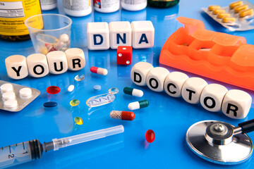 DNA pill on a blue table surrounded by various drugs and a vitamin. Wooden cubes with the...