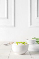 Bowl with sour cream and sliced green onion on white tile table