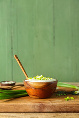 Bowl with sour cream and sliced green onion on brown wooden table near green wall