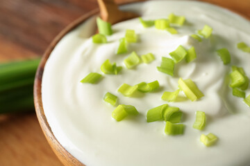 Bowl with sour cream and sliced green onion on brown wooden table