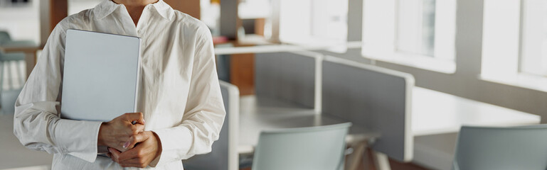 Attractive european business woman with laptop standing in modern office and looking at camera