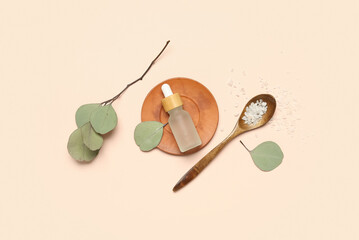 Bottle of cosmetic oil with sea salt and eucalyptus branch on beige background