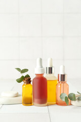 Composition with bottles of cosmetic oil, spa stones and eucalyptus branch on white tile