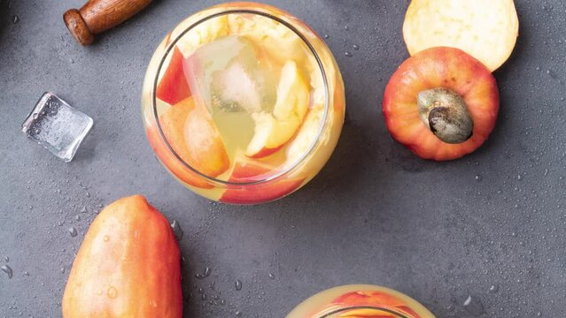 Brazilian cashew caipirinha in glasses with ice and fruit slices over stone background