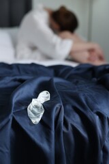 Woman sitting on bed and unrolled condom in bedroom, selective focus. Safe sex
