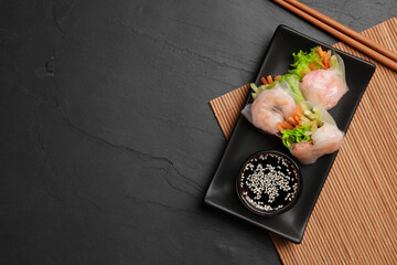 Tasty spring rolls served with soy sauce on dark grey textured table, flat lay. Space for text
