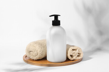 Fototapeta na wymiar Bottle with cosmetic product, rolled towel and loofah sponge on white background