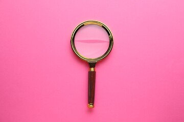 Magnifying glass on pink background, top view