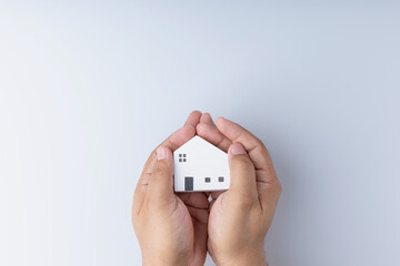 Real estate investing concepts, finance, banking, and saving money. A little wooden house model in hand, white background with copy space. Business of residence can make a profit in the future.