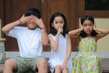 Three little beautiful children sitting and gesturing early education: see no evil, speak no evil,...