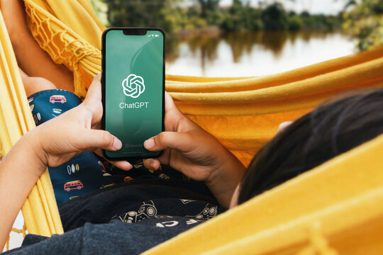 Child lying in hammock with ChatGPT artificial intelligence chatbot app on smartphone screen. Lake in the background. Rio de Janeiro, RJ, Brazil. May 2023