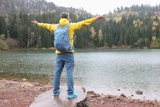 Man spreads hands to sides standing on stone against lake