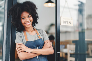 Smiling African American barista with apron standing welcomingly at a cafe door