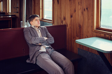 young man in a vintage railway car is sitting reading a book and looking out the window