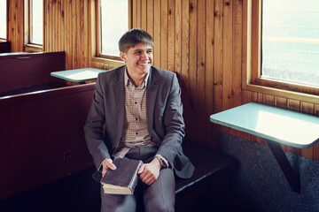 young man in a vintage railway car is sitting reading a book and looking out the window