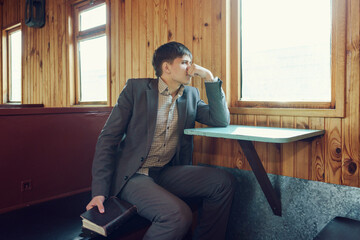 young man in a vintage railway car is sitting reading a book and looking out the window