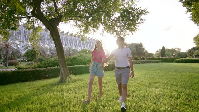 Lovely young couple strolling in city park while chatting and joking. Boyfriend and girlfriend holding hands and enjoying outdoor day in summer. High quality 4k footage Generative AI