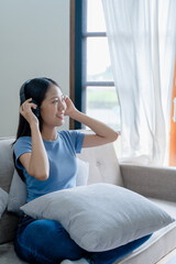 Peaceful girl in modern wireless headphones sit relax on comfortable couch listening to music, on cozy sofa, stress free concept.
