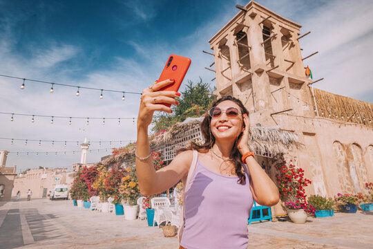 With her smartphone in hand, a happy girl tourist snaps a selfie to share with her followers from the charming old town of Dubai.